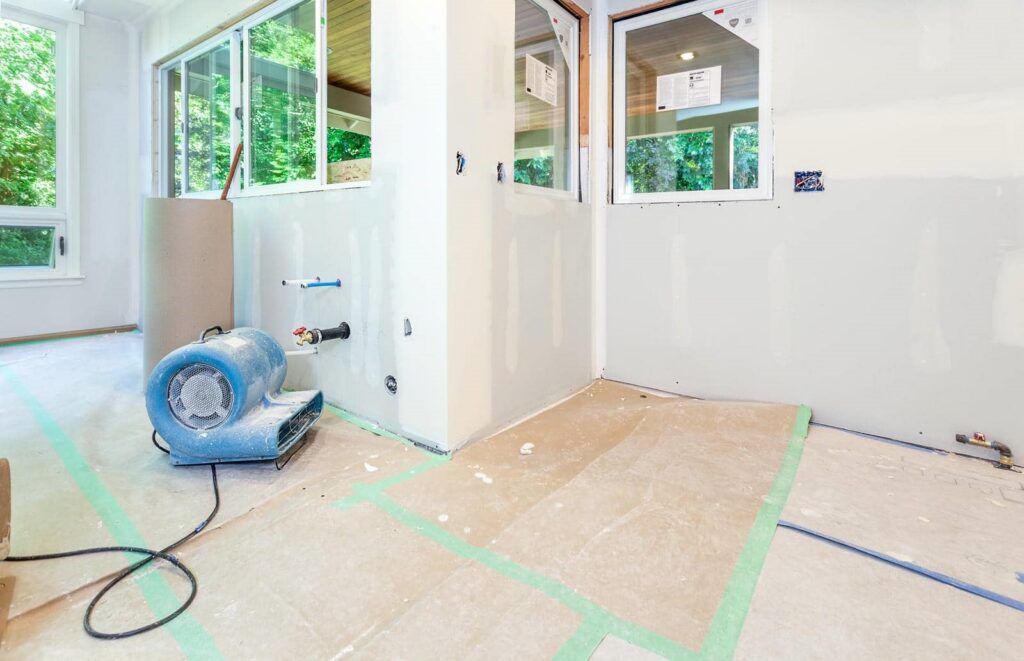 Unfinished room with drywall, windows, and a blue air mover on the floor.