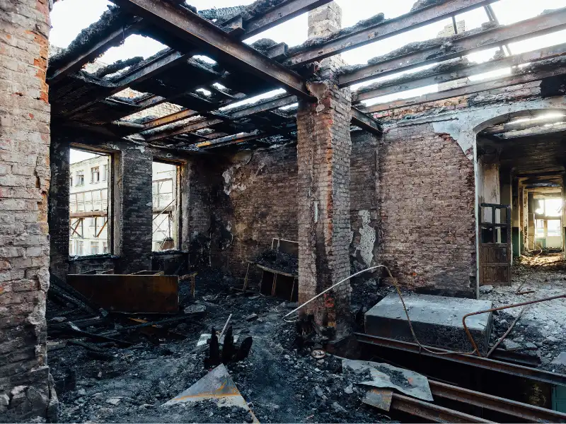 Burned-out interior of a brick building with charred debris and a partially collapsed roof.