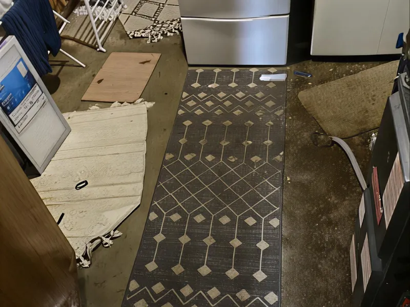 Worn kitchen floor with three different rugs and a stainless steel oven in the background.