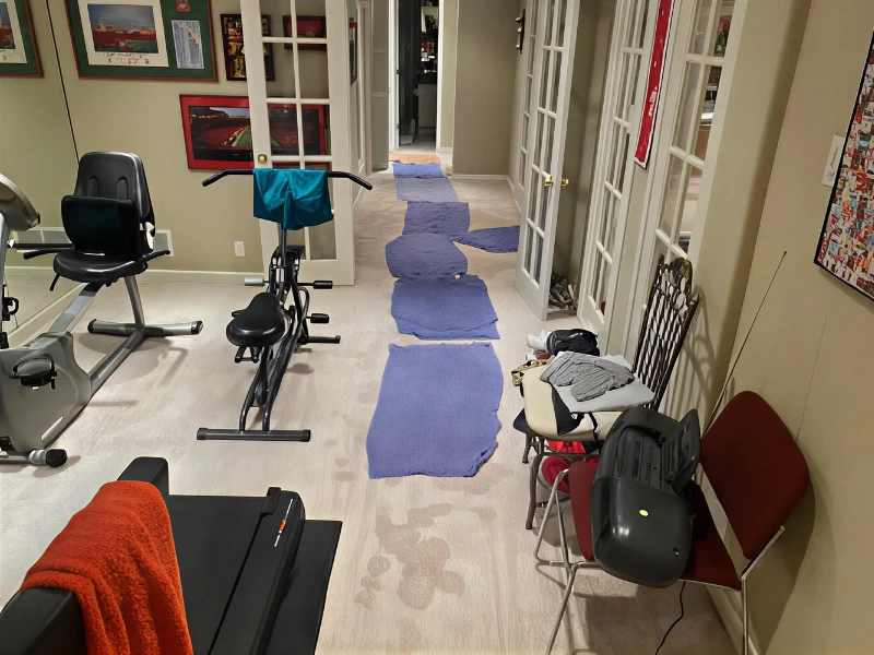 Exercise bikes and chairs with clothes in a narrow room with blue rugs on the floor.