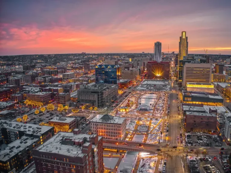 Cityscape of Omaha at sunset with illuminated buildings and streets covered in snow.